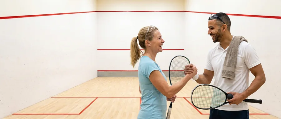 Twee spelers geven elkaar na de wedstrijd een hand op de squashbaan, de squashbril op het voorhoofd